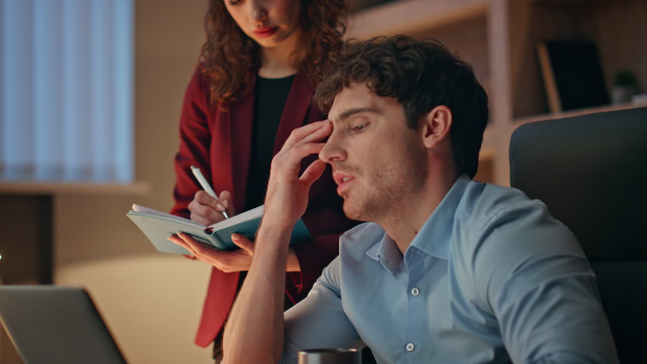 Chefe dando instruções à secretária que faz anotações no caderno em close-up.