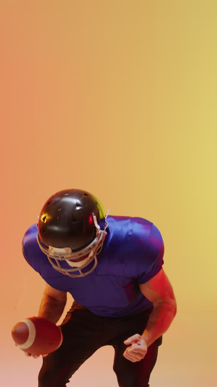 video vertical de un jugador de fútbol americano caucásico masculino sosteniendo la pelota, con iluminación naranja de neón