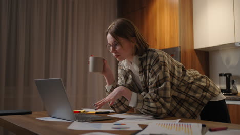 beautiful young woman working on laptop computer while sitting at the living room drinking coffee. happy casual beautiful woman working on a laptop. working at home with laptop and documents