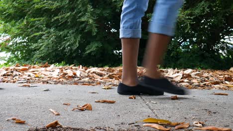 low angle and close up shot of feet walking by on a sidewalk surrounded by fallen leaves