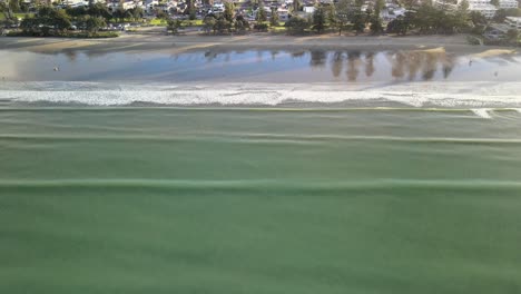 Drone-pan-up-of-relaxing-waves-along-the-beach-at-sunset