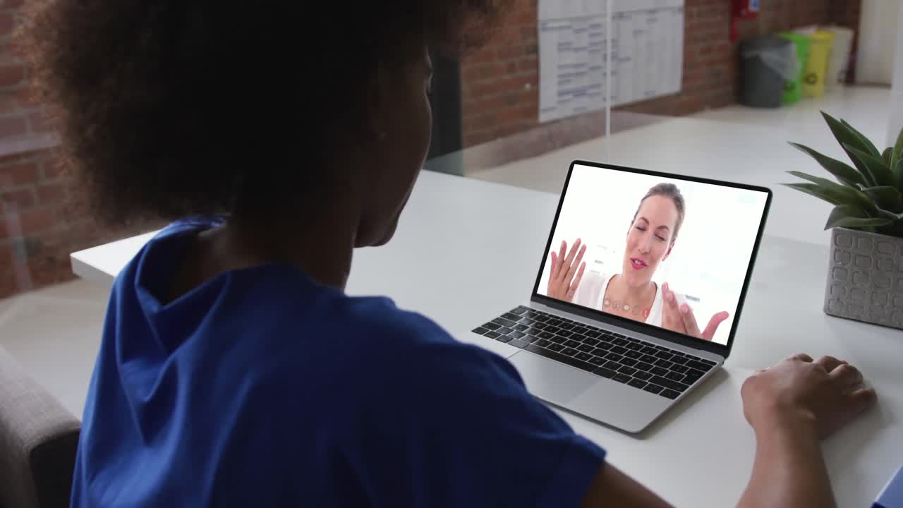 African american businesswoman sitting at desk using laptop having video call with female colleague
