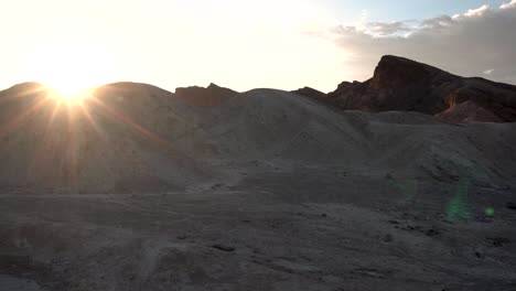 Sun-shining-behind-compacted-sand-dunes-in-Death-Valley,-California,-Aerial-approach-shot