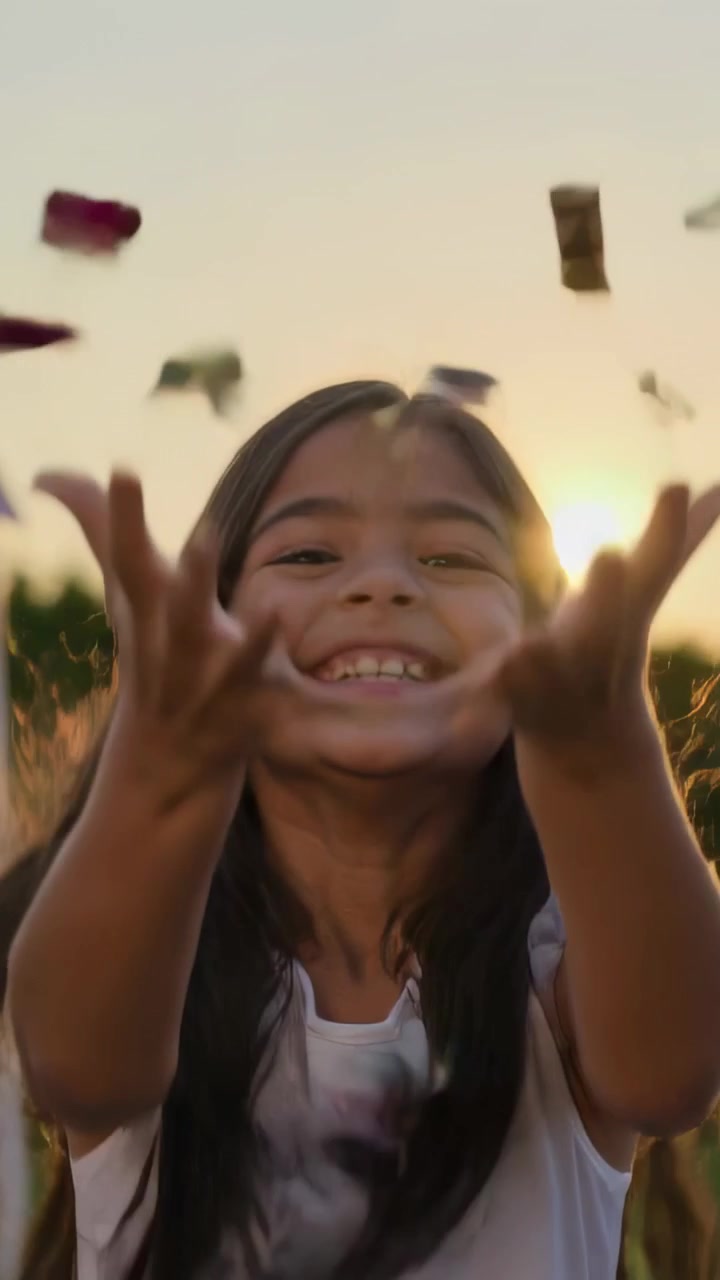 Video verticale: Bambino sorridente che alza le braccia, lancia coriandoli al tramonto in un prato, con un tutù pastello.