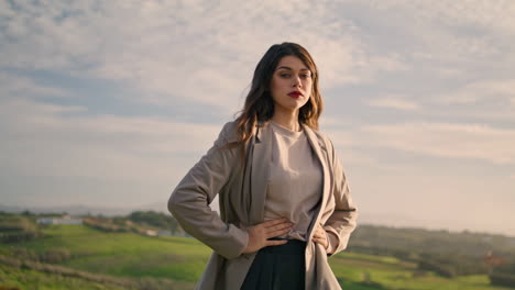 elegant girl posing confidently in front cloudy sky. model standing green hill.