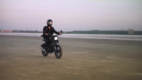 unrecognizable young biker in helmet and jacket, man is riding at sport motorbike. wind blowing, water front