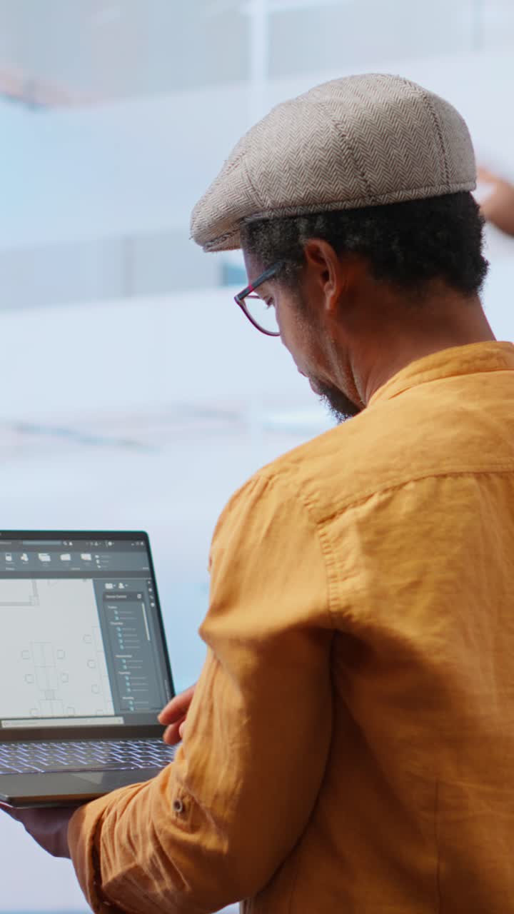 Hombre Afroamericano Discutiendo Planos Arquitectónicos en un Portátil
