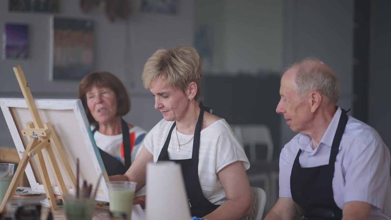 캔버스에 그림을 그리는 즐거운 고령 친구들의 높은 각도 전망. 그룹과 함께 그림을 그리는 동안 미소 짓는 고령 여성. 함께 그림 수업에 참석하는 고령 남자들이 미술 수업에서 재미있는 그림을 그리고 있습니다.