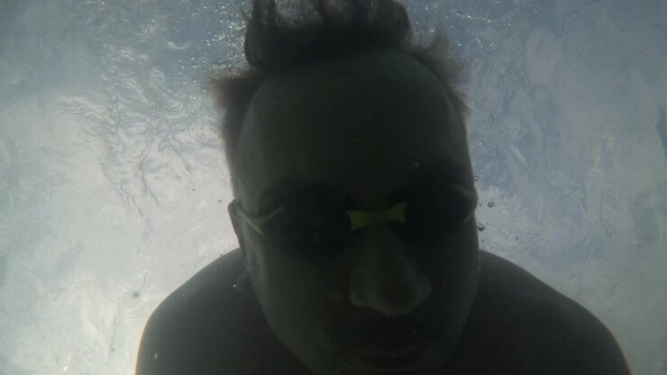 Slow motion underwater close-up portrait of a man wearing swim goggles