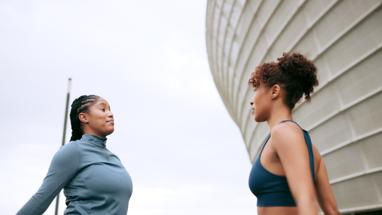 Two women stretching outdoors near a stadium