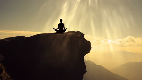 silhouette of a person meditating on a mountain cliff at sunrise