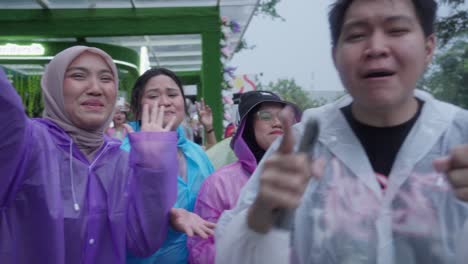 happy group of concert goers dancing and singing in the rain. people wearing colorful ponchos at an outdoor music festival in bogor, indonesia.