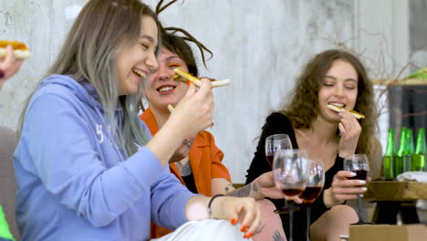 happy female friends eating pizza, drinking wine and talking at home