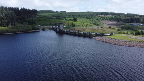 Alwen-reservoir-Welsh-woodland-lake-water-supply-aerial-view-concrete-dam-countryside-park-reverse-descending-tilt-up-shot