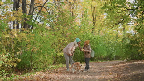 mother and child enjoy peaceful moment in colorful forest, gently interacting with dog on leash, surrounded by golden leaves and trees on quiet path during autumn afternoon walk outdoors