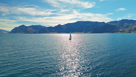 aerial pullback as sailboat sits in middle of sun ray reflecting sparkling on water