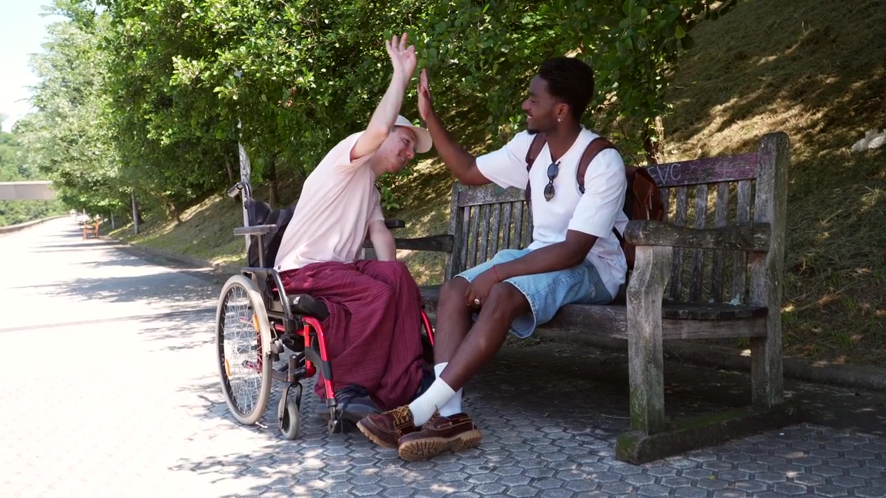 Two Young Men Talking and High-Fiving on a Park Bench