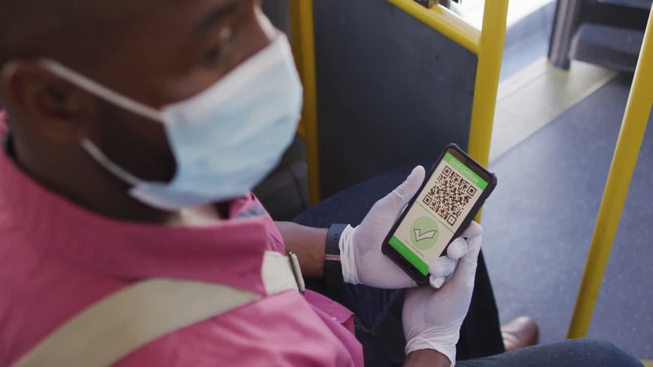 Hands of african american man wearing face mask, using smartphone with covid passport in bus