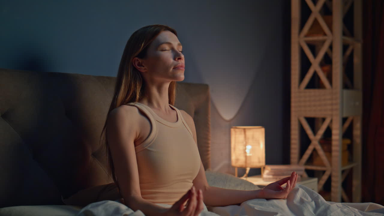 Girl meditating late evening preparing to sleep in bedroom. Woman closing eyes