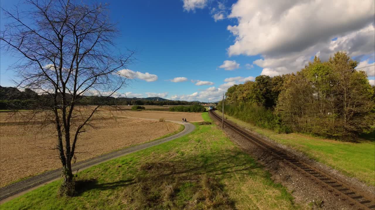 Train moving through Austrian farmland with blue skies above, showcasing the beauty of rural transport in autumn