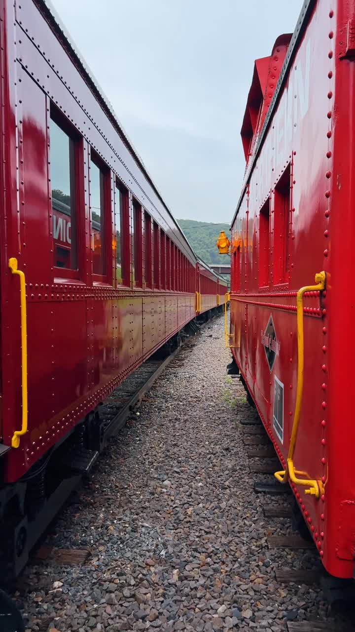Boston, USA, 8 May 2025: Perspective view along side of red passenger train cars. View from ground level looking down the side of red wooden train carriages on curved tracks toward mountains