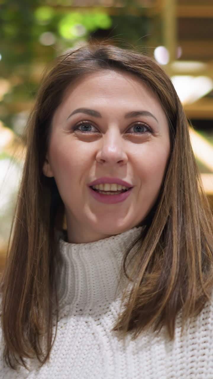 primer plano de una joven mujer caucásica en un suéter blanco, sonriendo sutilmente a la cámara frente a una tabla de salida del aeropuerto borrosa