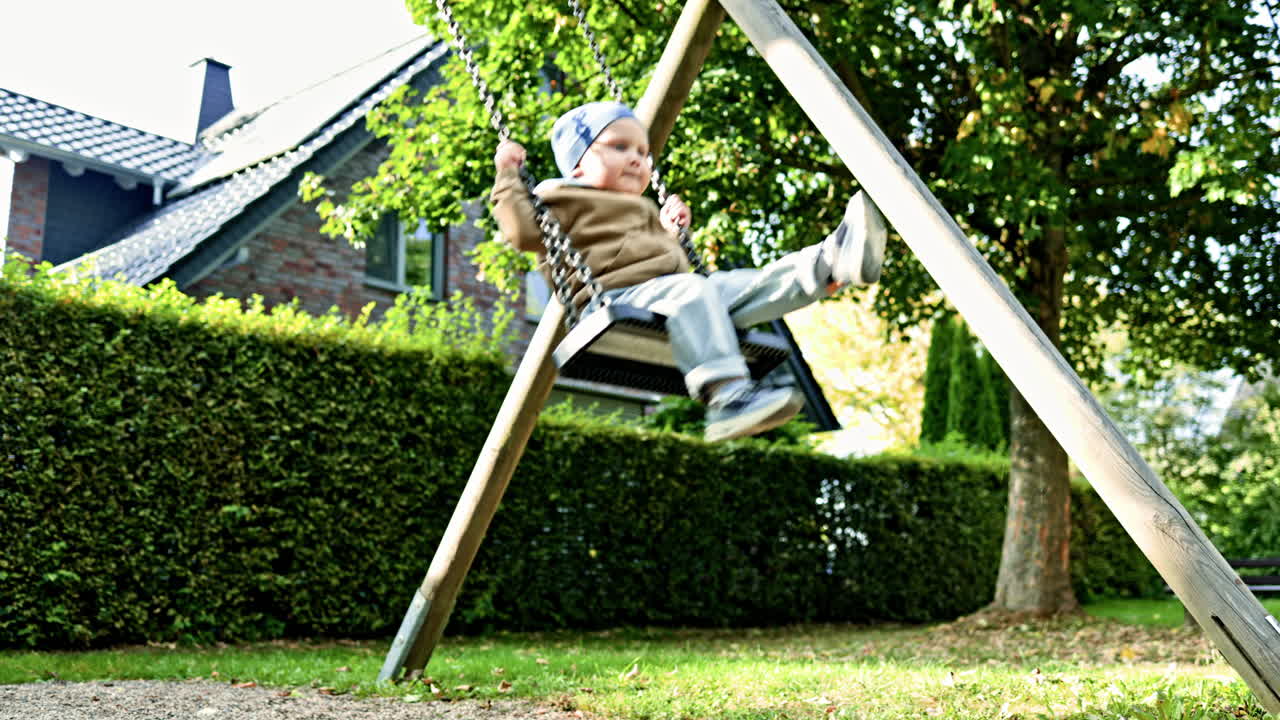 Boy 2 years old swings on a swing in a city park. Toddler swings on a playground. Child having fun and playing in the park. Children's swing on a playground