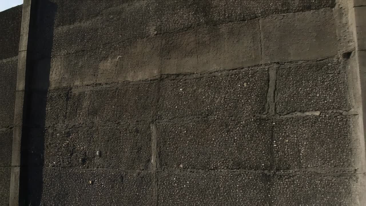 Câmera panorâmica recuando para revelar a parede de concreto com pedras no aterro, mostrando pilastras e sombra