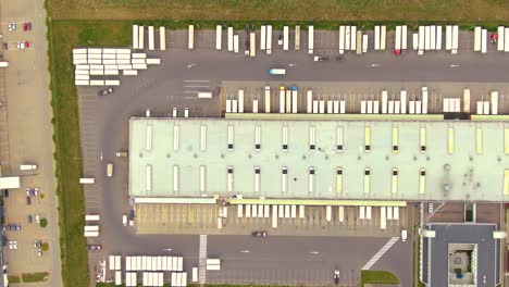 aerial top down view of the big logistics park with warehouses, loading hub and a lot of semi trucks with cargo trailers awaiting for loading unloading goods on ramps