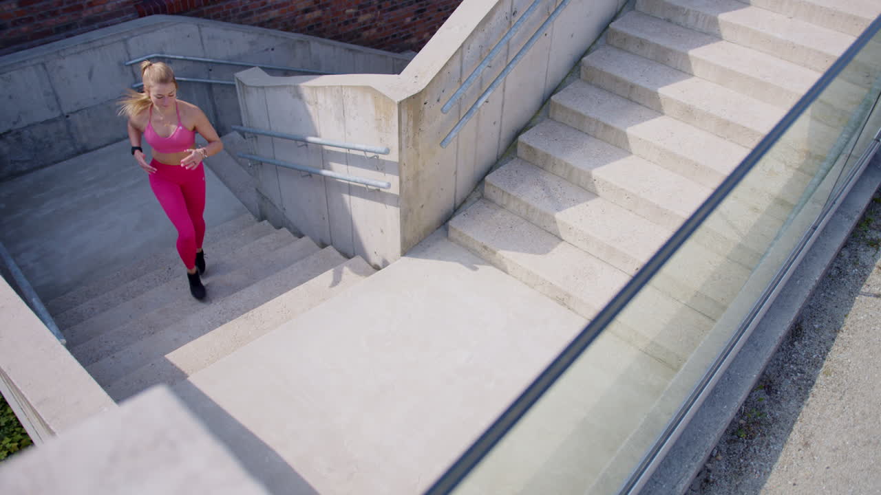 Fit young blonde woman in pink workout clothes runs up stairs outdoors