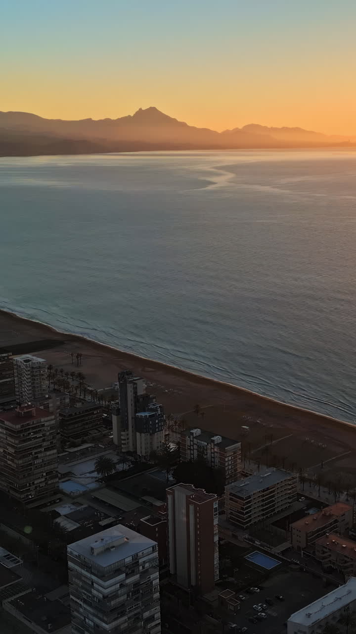 Aerial drone view of the Mediterranean Sea and the city of Alicante, Spain at sunset. Vertical