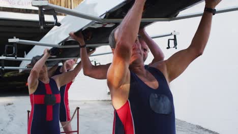 four senior caucasian men and women carrying a rowing boat together