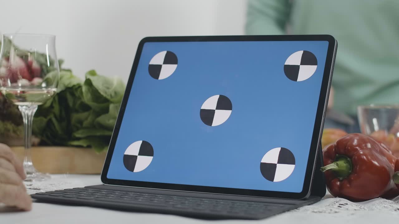 Close-up of blue screen laptop with blurred senior women cooking healthful dietary food in kitchen at home. Unrecognizable Caucasian retirees using online recipe from web-site. Cinema 4k ProRes HQ.