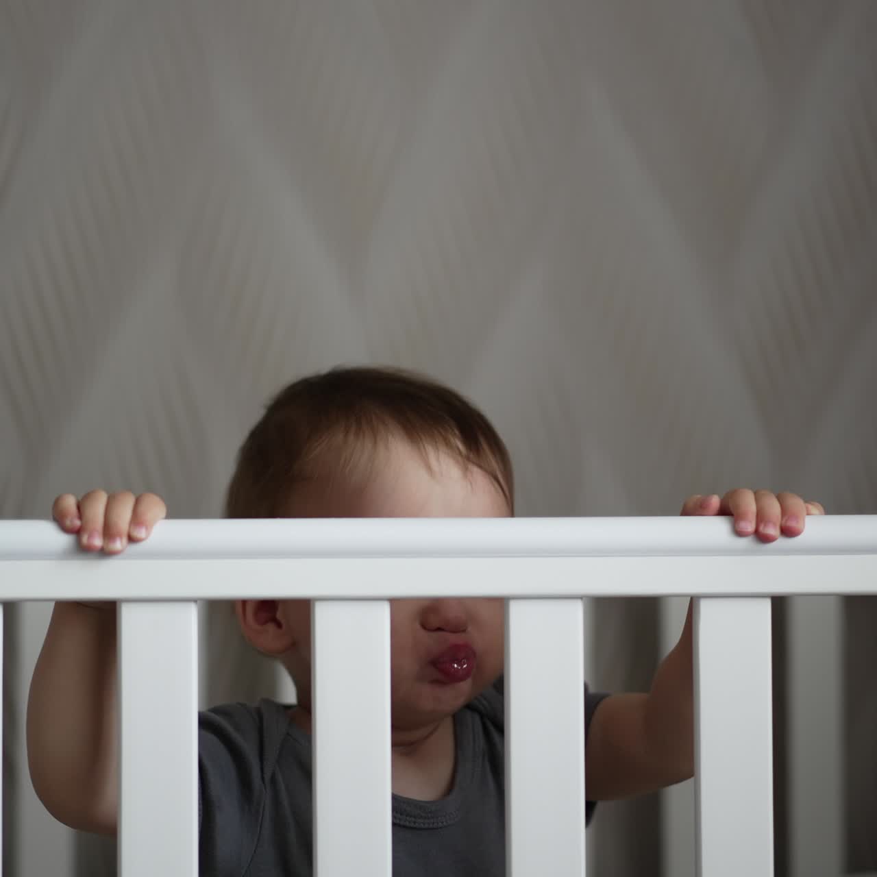 Little boy standing up and sitting down in the cot. Adorable Caucasian child being active after waking up