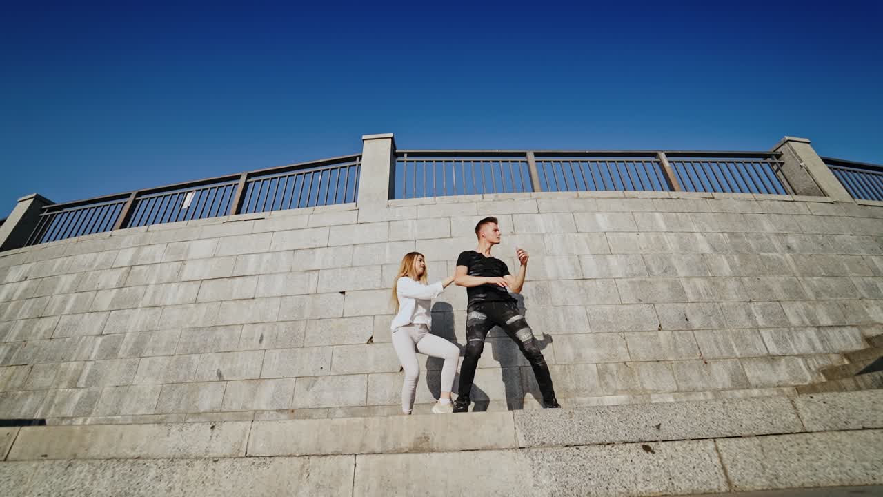 Passion dance of young couple. Talented teenage boy and girl performing modern dance near the grey wall outdoors. View from below.