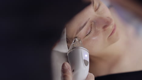 esteticista hace a la mujer rf lifting procedimiento de cosmetología de la cara y los ojos mascarilla de colágeno en el spa