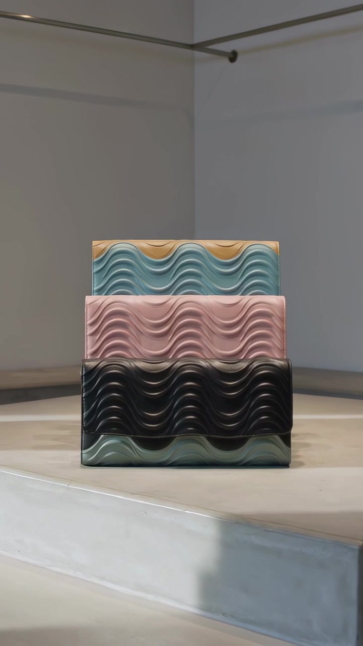 Video verticale: Telecamera in movimento che mostra tre pochette a onda su piedistalli in una galleria, rivelando colore e texture.