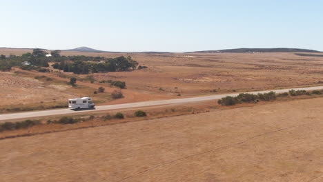 Fast-drone-approaching-shot-of-Campervan-driving-on-an-empty-road-on-a-sunny-day