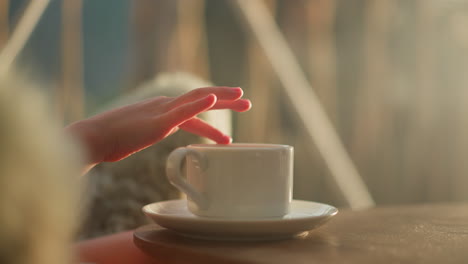 child move finger along rim of cup. kid sits at breakfast table with cup of warm tea beginning new day on blurred background. morning routine