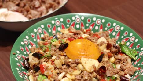 a vibrant thai rice meal is presented on a wooden table, featuring minced meat, egg yolk, vegetables, and seaweed soup under bright indoor lighting with close-up camera angles