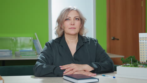 professional lady closes book and casually drops pen on cover as it rolls toward miniature building model on desk, set in bright office space with organized shelves and modern decor elements