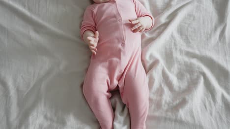 Baby-lying-on-bed-and-moving-arms-and-legs-wearing-bodysuit,-top-down-view