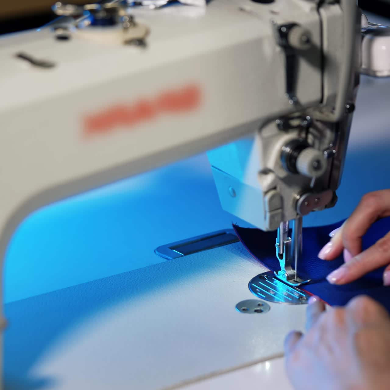 Woman works at sewing machine. Female hands moving cloth while needle of the sewing machine doing stitches in atelier