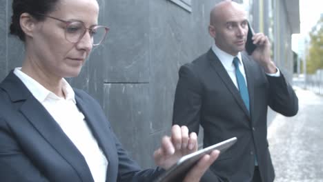 business team standing at office building outside, using tablet, laptop and mobile phone