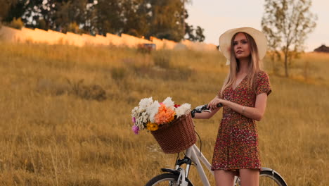 Slow-motion-sexy-beautiful-woman-with-a-bike-in-a-hat-and-a-light-summer-dress-comes-with-flowers-in-a-basket-and-smiles.