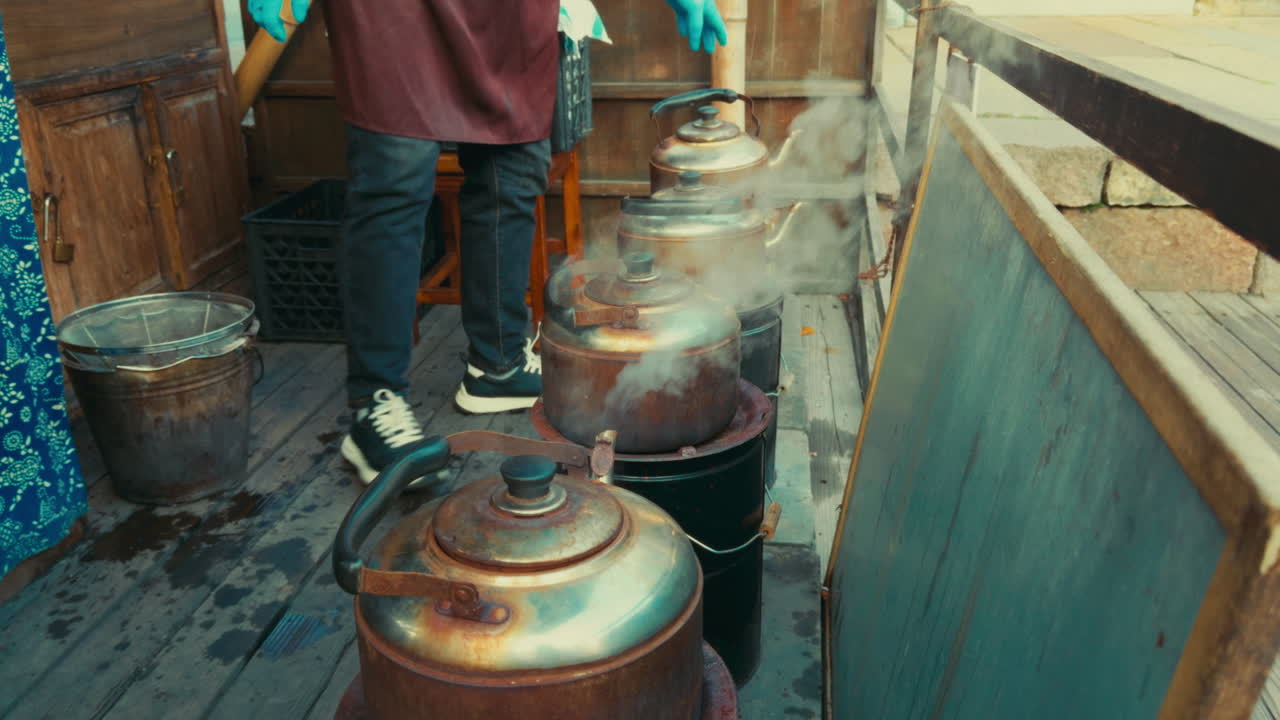 A person is seen tending to large steaming kettles in a rustic setting in Wuzhen, China.