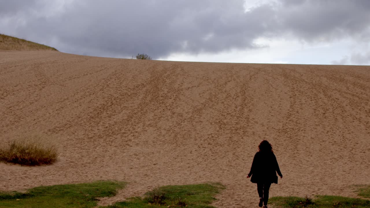 Donna di mezza età che sale sulla Dune Climb presso il Sleeping Bear Dunes National Lakeshore nel Michigan in una giornata autunnale, ripresa video stabile e ampia