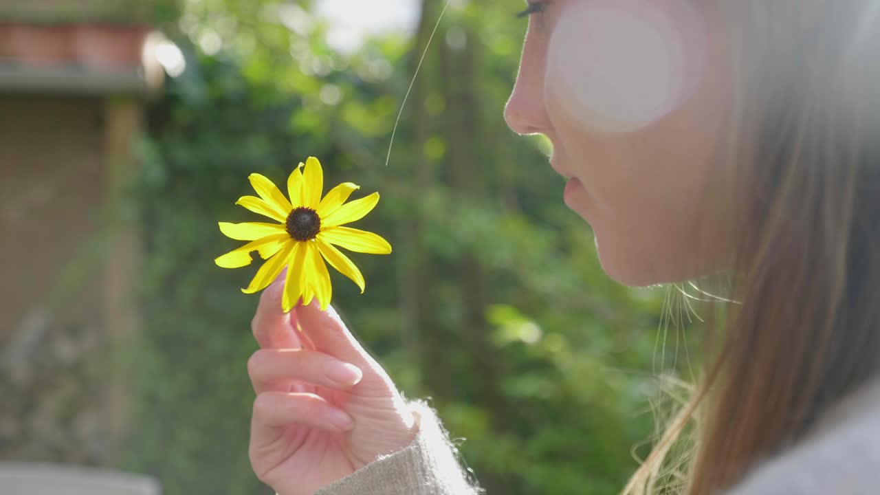 Young woman spins yellow daisy in fingers outside, lens flare,close-up