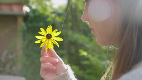 young woman spins yellow daisy in fingers outside, lens flare,close-up