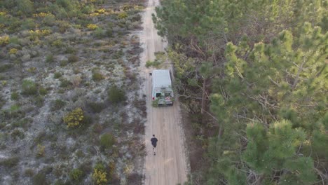 man running alongside a green travel camper van down a dirt road with a forest next to them at sunset in nazare portugal